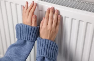 Persona comprobando con las manos un radiador que no se calienta en su vivienda durante el invierno, imagen utilizada por Triergy en su guía sobre problemas de calefacción y mantenimiento de radiadores.